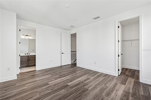 unfurnished bedroom with a spacious closet, connected bathroom, dark hardwood / wood-style floors, and a closet