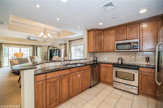 kitchen with crown molding, appliances with stainless steel finishes, sink, a raised ceiling, and dark stone counters