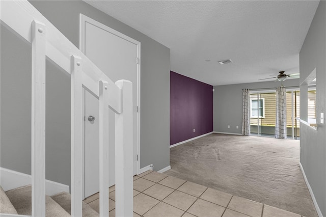 empty room featuring visible vents, a ceiling fan, light carpet, light tile patterned flooring, and baseboards