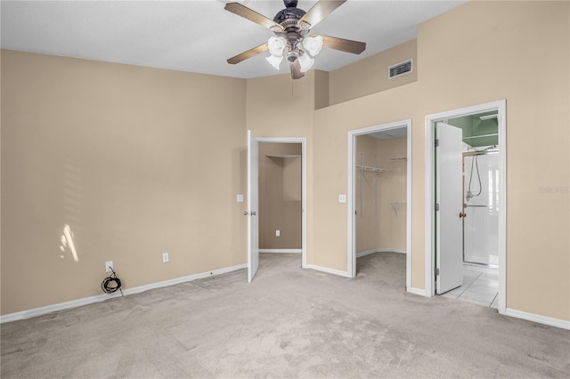 unfurnished bedroom with a closet, ceiling fan, connected bathroom, light colored carpet, and a walk in closet