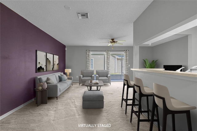 living area featuring light colored carpet, visible vents, ceiling fan, a textured ceiling, and baseboards