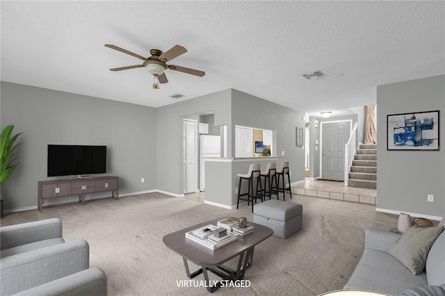 living area with light colored carpet, visible vents, stairway, a ceiling fan, and a textured ceiling