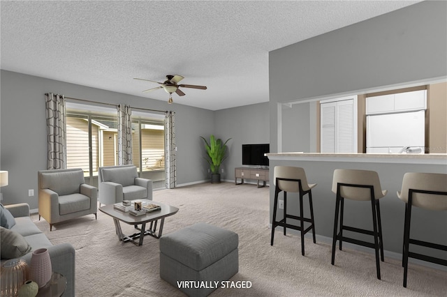 living area with a textured ceiling, baseboards, a ceiling fan, and light colored carpet