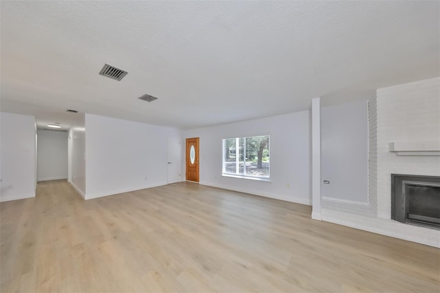 unfurnished living room with light hardwood / wood-style flooring, a fireplace, brick wall, and a textured ceiling