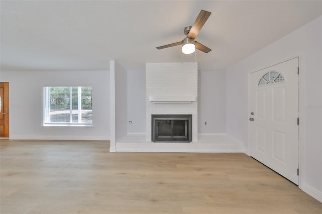 unfurnished living room with ceiling fan, light hardwood / wood-style floors, brick wall, and a brick fireplace