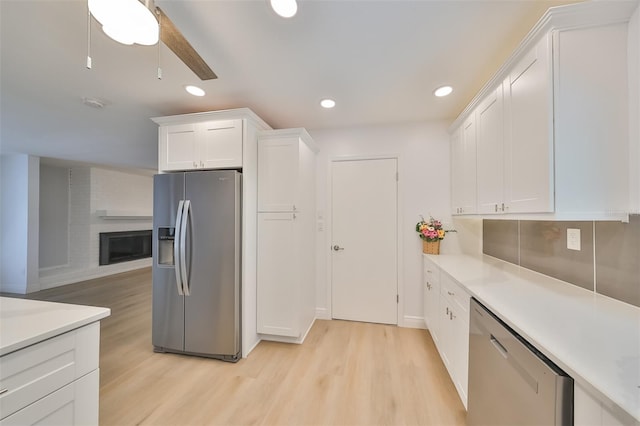 kitchen with a brick fireplace, appliances with stainless steel finishes, light hardwood / wood-style flooring, tasteful backsplash, and white cabinets