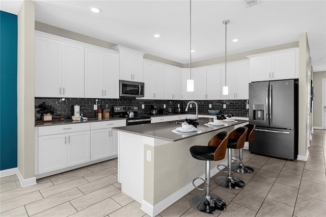 kitchen featuring appliances with stainless steel finishes, backsplash, an island with sink, and white cabinetry