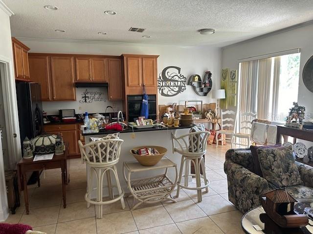 kitchen featuring a textured ceiling, a kitchen bar, light tile flooring, black appliances, and ornamental molding