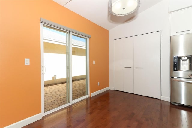 unfurnished bedroom with stainless steel refrigerator with ice dispenser, dark hardwood / wood-style flooring, and lofted ceiling