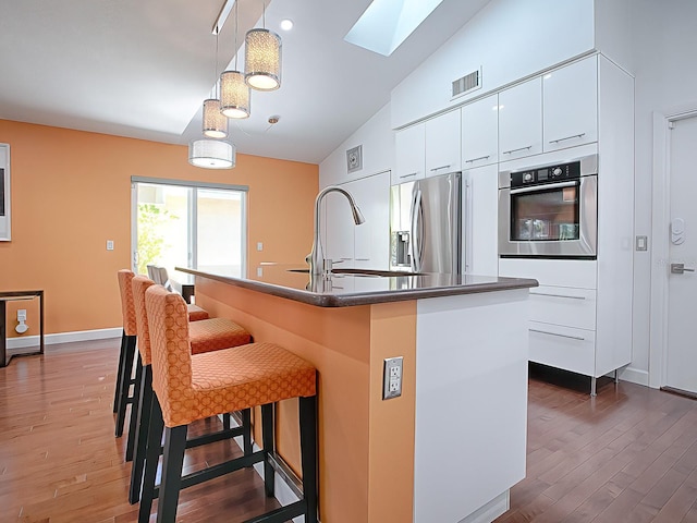 kitchen featuring pendant lighting, a kitchen island with sink, sink, appliances with stainless steel finishes, and white cabinetry