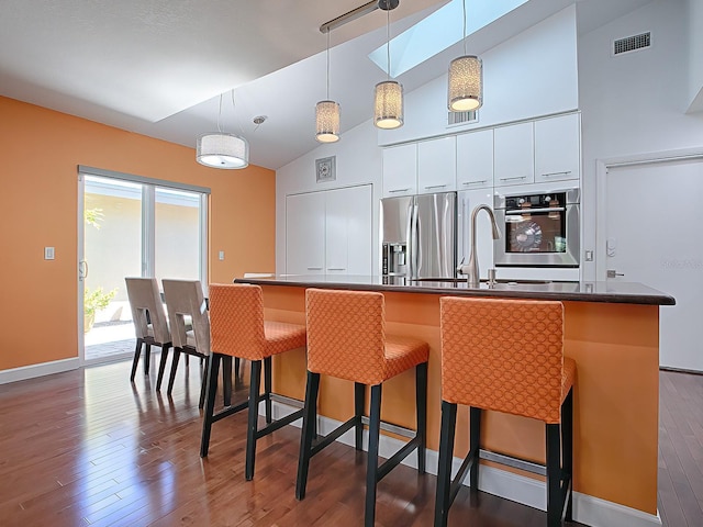 kitchen featuring appliances with stainless steel finishes, dark hardwood / wood-style flooring, vaulted ceiling, pendant lighting, and white cabinets