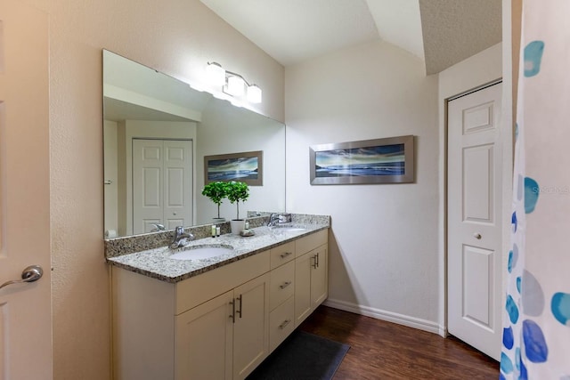 bathroom with dual bowl vanity, hardwood / wood-style floors, and lofted ceiling