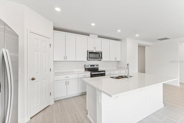 kitchen with white cabinetry, appliances with stainless steel finishes, sink, and a kitchen island with sink