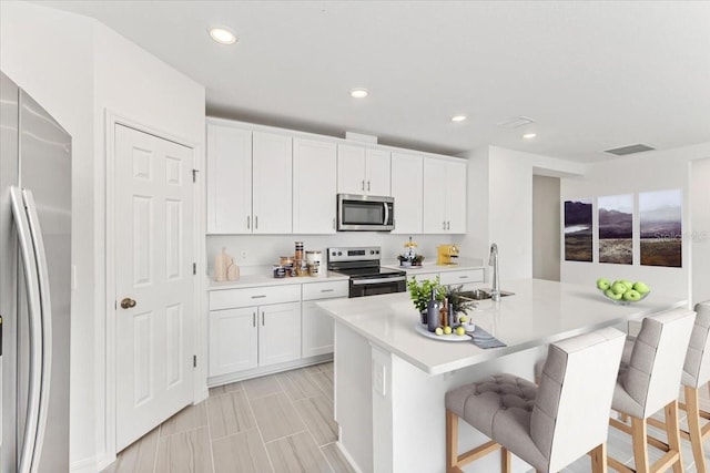 kitchen featuring a breakfast bar, sink, white cabinetry, an island with sink, and stainless steel appliances