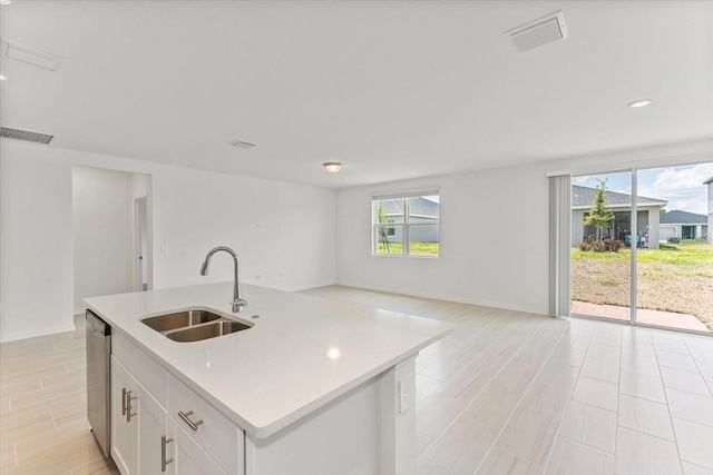 kitchen featuring sink, white cabinetry, stainless steel dishwasher, a kitchen island with sink, and light hardwood / wood-style floors