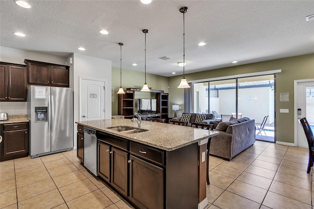 kitchen featuring light stone counters, hanging light fixtures, stainless steel appliances, a center island with sink, and sink