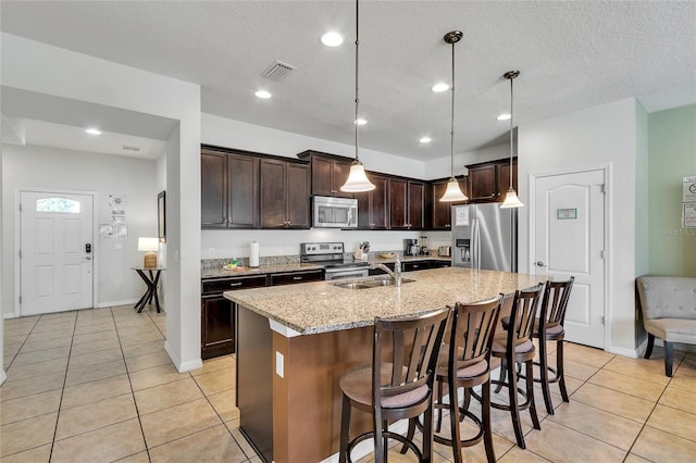 kitchen featuring hanging light fixtures, appliances with stainless steel finishes, an island with sink, and a breakfast bar area