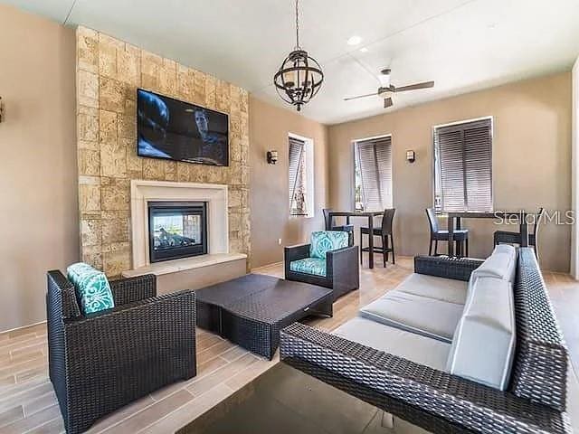 living room with ceiling fan with notable chandelier and a large fireplace