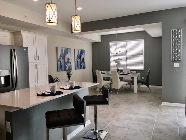 kitchen featuring a breakfast bar area, white cabinets, decorative light fixtures, and light tile floors