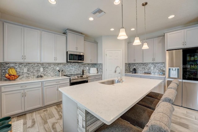 kitchen featuring backsplash, pendant lighting, stainless steel appliances, and an island with sink