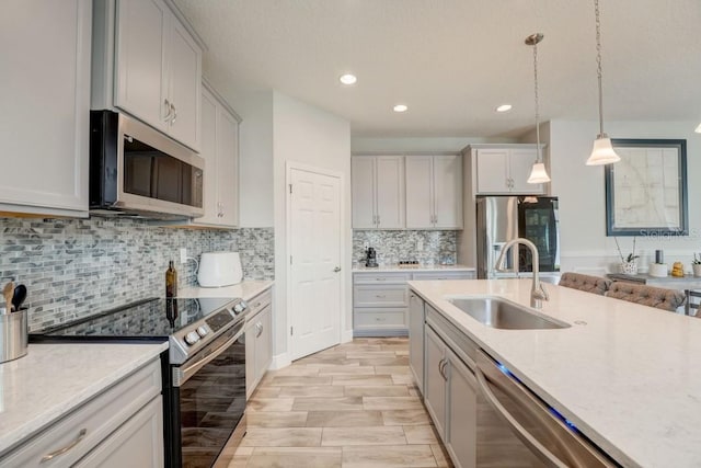 kitchen with pendant lighting, backsplash, stainless steel appliances, sink, and light stone counters