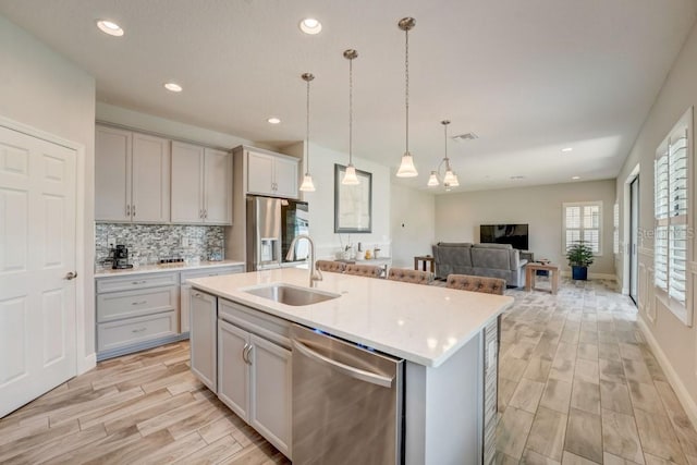 kitchen with hanging light fixtures, backsplash, stainless steel appliances, sink, and an island with sink