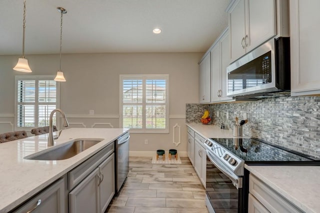 kitchen with pendant lighting, light stone countertops, backsplash, appliances with stainless steel finishes, and sink