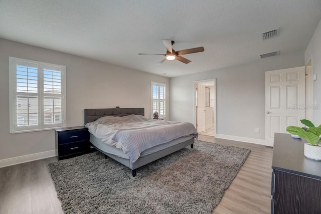 bedroom with a textured ceiling, connected bathroom, ceiling fan, and hardwood / wood-style floors