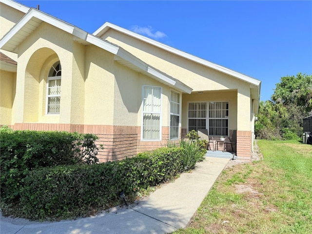 entrance to property with brick siding, stucco siding, and a yard