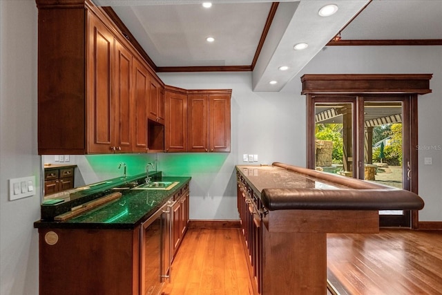 kitchen with light hardwood / wood-style flooring, ornamental molding, kitchen peninsula, sink, and dark stone counters