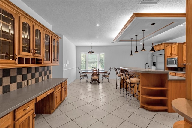 kitchen featuring a kitchen breakfast bar, built in appliances, hanging light fixtures, and a textured ceiling