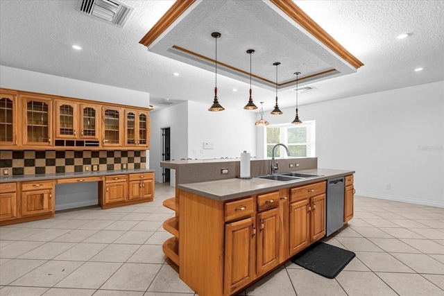 kitchen featuring a tray ceiling, backsplash, stainless steel dishwasher, sink, and an island with sink