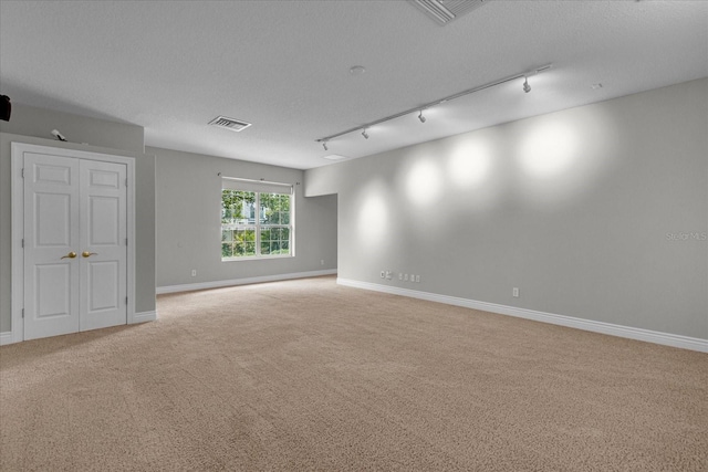 carpeted empty room featuring a textured ceiling and track lighting