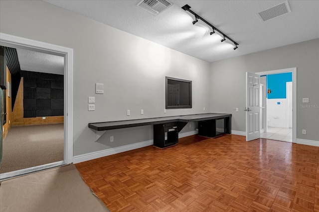 unfurnished living room with light parquet floors, built in desk, track lighting, and a textured ceiling