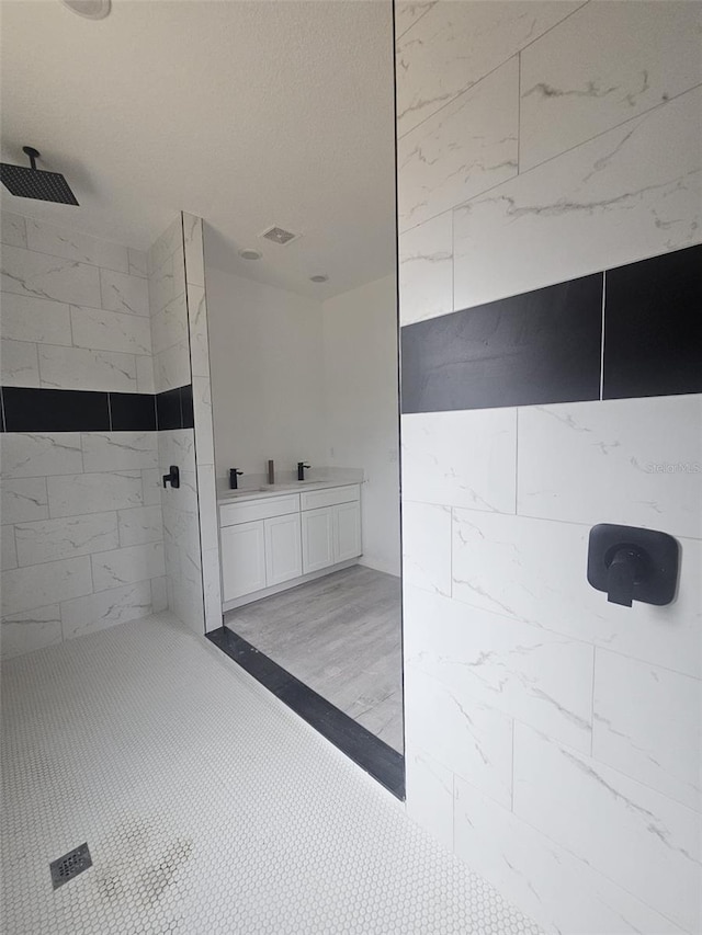 bathroom with vanity, a tile shower, and wood-type flooring