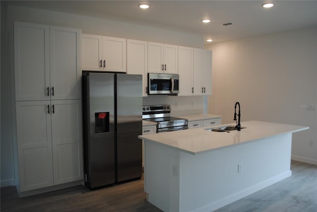 kitchen featuring appliances with stainless steel finishes, a kitchen island with sink, a sink, and dark wood-type flooring