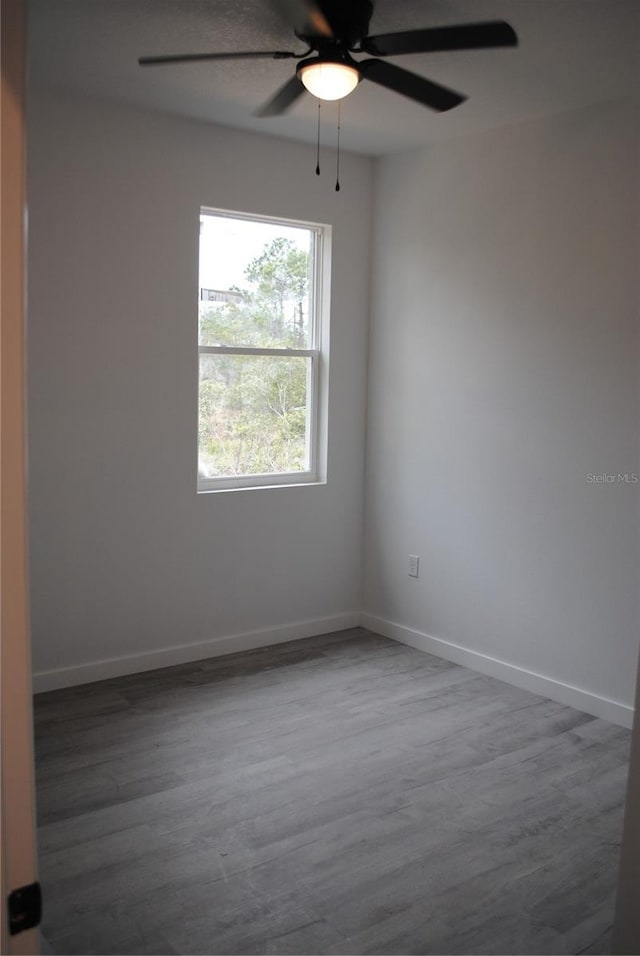 empty room with ceiling fan, wood finished floors, and baseboards