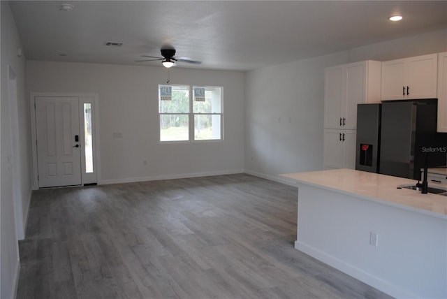 kitchen with light countertops, visible vents, black fridge with ice dispenser, white cabinetry, and light wood-type flooring