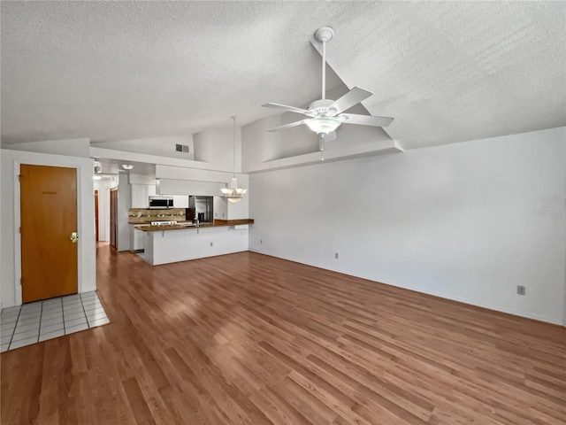 unfurnished living room featuring high vaulted ceiling, light tile flooring, ceiling fan with notable chandelier, and a textured ceiling