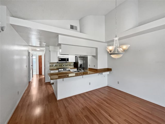 kitchen with kitchen peninsula, hanging light fixtures, stainless steel appliances, hardwood / wood-style flooring, and white cabinets