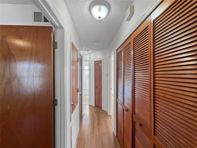 corridor with light hardwood / wood-style flooring and a textured ceiling