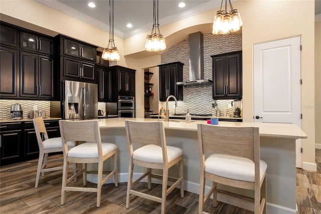 kitchen with tasteful backsplash, an island with sink, wall chimney range hood, and stainless steel fridge with ice dispenser