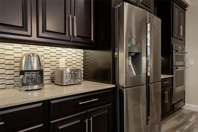 kitchen with light stone countertops, backsplash, appliances with stainless steel finishes, dark brown cabinets, and hardwood / wood-style flooring