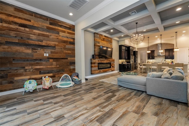 living room with wooden walls, ornamental molding, a chandelier, beam ceiling, and coffered ceiling