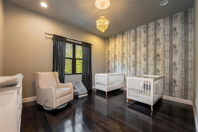 bedroom featuring an inviting chandelier, a nursery area, and dark wood-type flooring