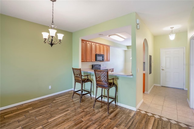 kitchen featuring light tile flooring, a breakfast bar area, stainless steel electric stove, a chandelier, and pendant lighting