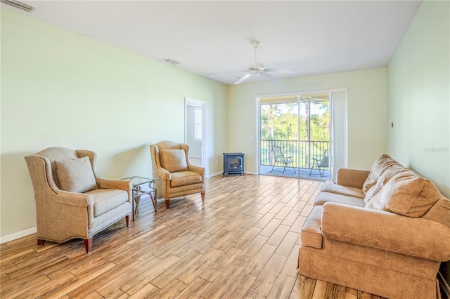 sitting room with a wood stove, ceiling fan, and light hardwood / wood-style floors