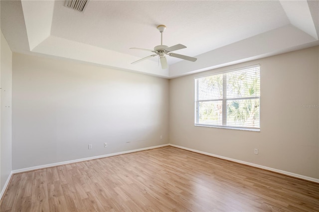 spare room with a raised ceiling, ceiling fan, and light wood-type flooring