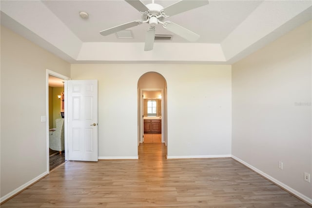 empty room with a raised ceiling, light hardwood / wood-style flooring, and ceiling fan