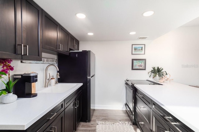 kitchen with sink, refrigerator, electric range, light hardwood / wood-style flooring, and dark brown cabinets